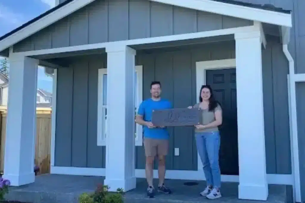 Two people holding a sign on the porch of a home in Mukilteo.